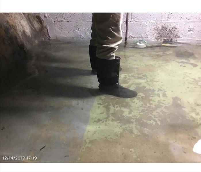 Visible feet and legs of a person standing in water on a basement floor